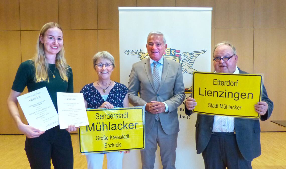 14 Kommunen verleiht Innenminister Thomas Strobl (2.v.re.) Zusatzbezeichnungen. Doch kaum einer der nach Stuttgart Gereisten kann schon ein vorläufiges Ortsschild vorweisen, wie es der OB-Stellvertreter Günter Bächle für das Etterdorf Lienzingen und die Landtagsabgeordnete Stefanie Seemann für die Senderstadt Mühlacker präsentieren. Judith Jäkel (li.), Mitarbeiterin der Gemeinderatsgeschäftsstelle der Stadt Mühlacker, hält die Urkunden in Händen, die vom Erfolg des Mühlacker Antrags zeugen. Foto: Stadt Mühlacker