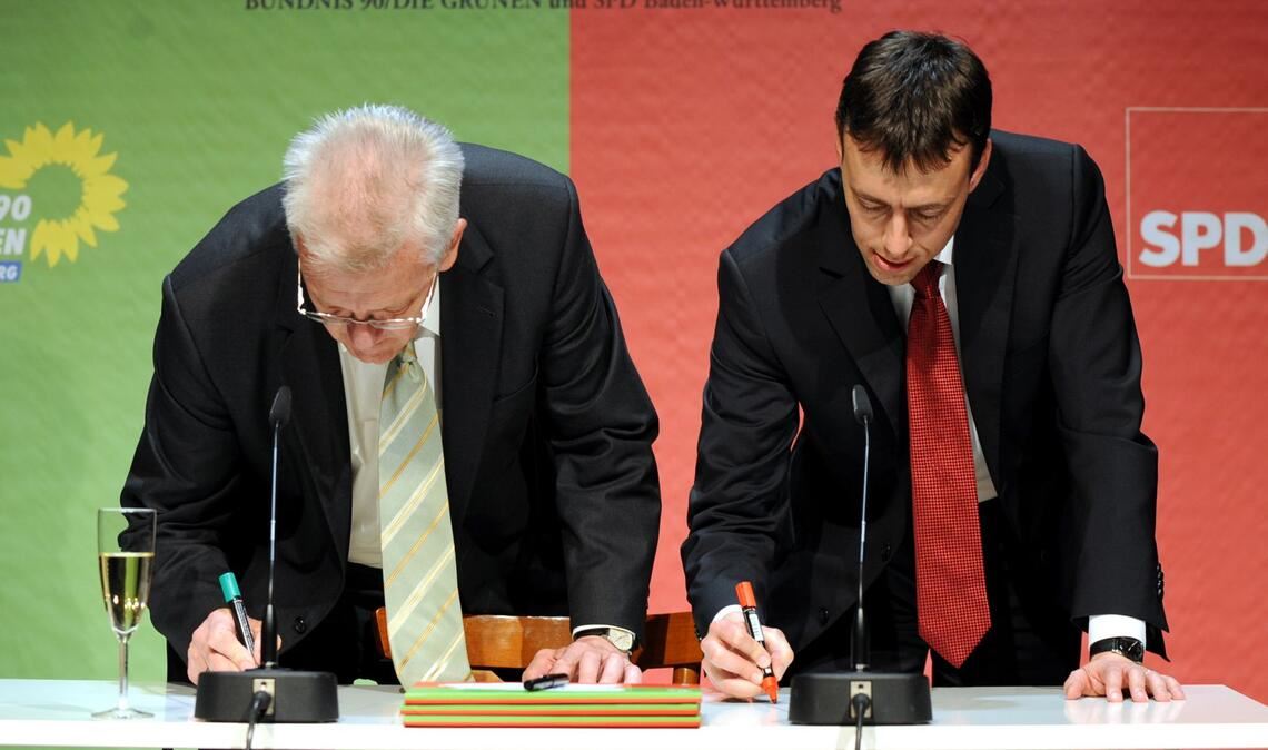 2011: Der designierte baden-württembergische Ministerpräsident Winfried Kretschmannund der designierte Minister für Finanzen und Wirtschaft, Nils Schmid (SPD), schreiben  gemeinsam ihre Namen auf den Tisch. (Archivbild).