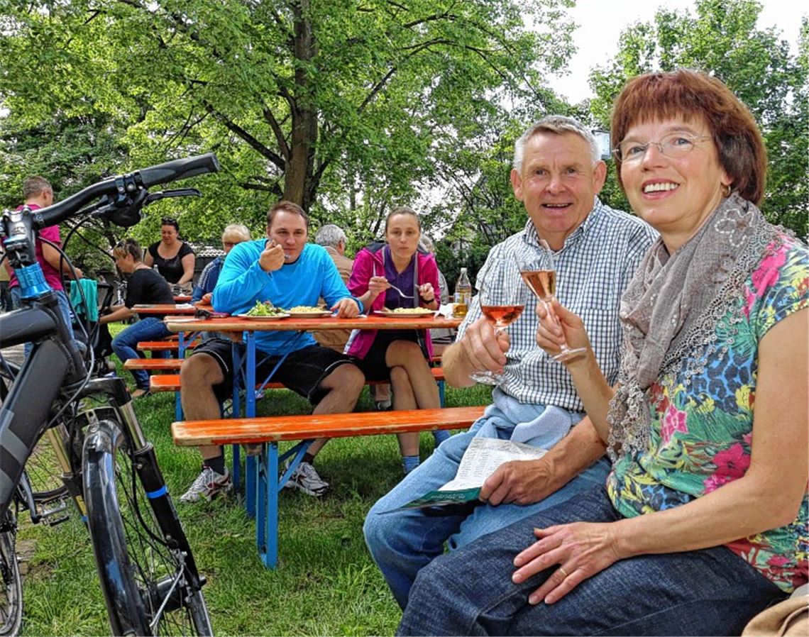 Agnes und Dieter Heck (v. re.) genießen auf dem Dorfplatz im Schatten des Kirchturmes Sekt und Wein der WG Sternenfels. Viele Besucher lockt das Essensangebot. Foto: Hansen