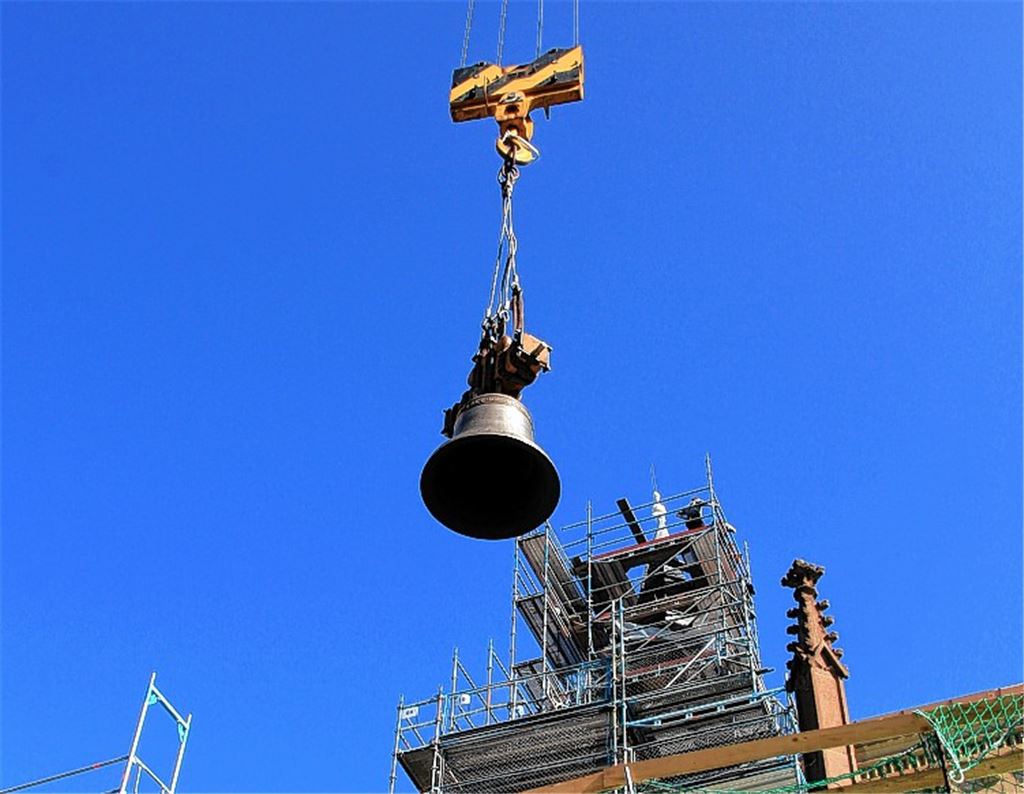 Am Kranseil schwebt die neue Glocke auf das Dach, wo Gerhard Ufer (li.) und Peter Westermann von der Herstellerfirma Bachert dafür sorgen, dass sie absolut waagerecht ausgerichtet ist.