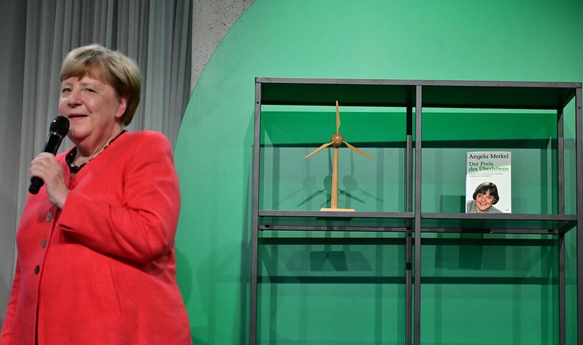 Angela Merkel (CDU), Bundeskanzlerin a.D. und ehemalige Bundesumweltministerin, spricht auf der Bühne beim Festakt "Seit 40 Jahren NaturVerbunden" zum 40. Jubiläum des Bundesumweltministeriums im Café "Moskau", während im Hintergrund ihr Buch mit dem Titel „Der Preis des Überlebens“ zu sehen ist.