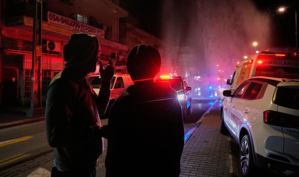 Anwohner beobachten die Arbeit der Rettungskräfte am Ort eines Raketeneinschlags in Tel Aviv.