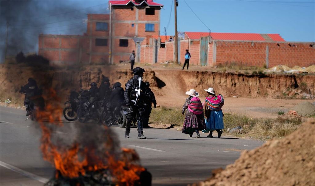 Anwohner gehen an einem Polizisten vorbei, der in Bolivien an einer brennenden Barrikade steht.