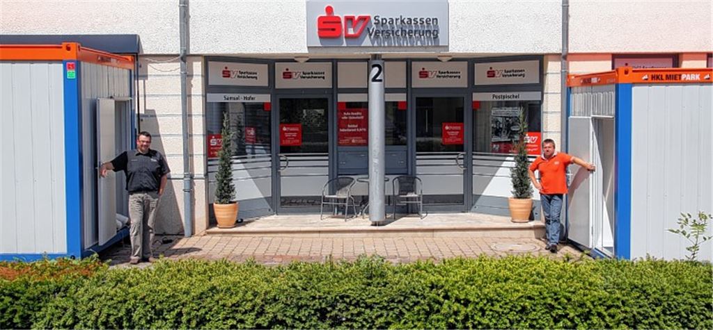 Arbeiten im Provisorium: Vor der Tür der eigentlichen Geschäftsstelle, die am 1. Juni überflutet wurde, betreuen Jörg Postpischel (re.) und Jens Neumeister in zwei Containern ihre Kunden, darunter ebenfalls viele Opfer des Hochwassers. In den regulären Räumen laufen derweil noch immer auf Hochtouren die Hochleistungstrockner, um Wände und Böden zu entfeuchten.