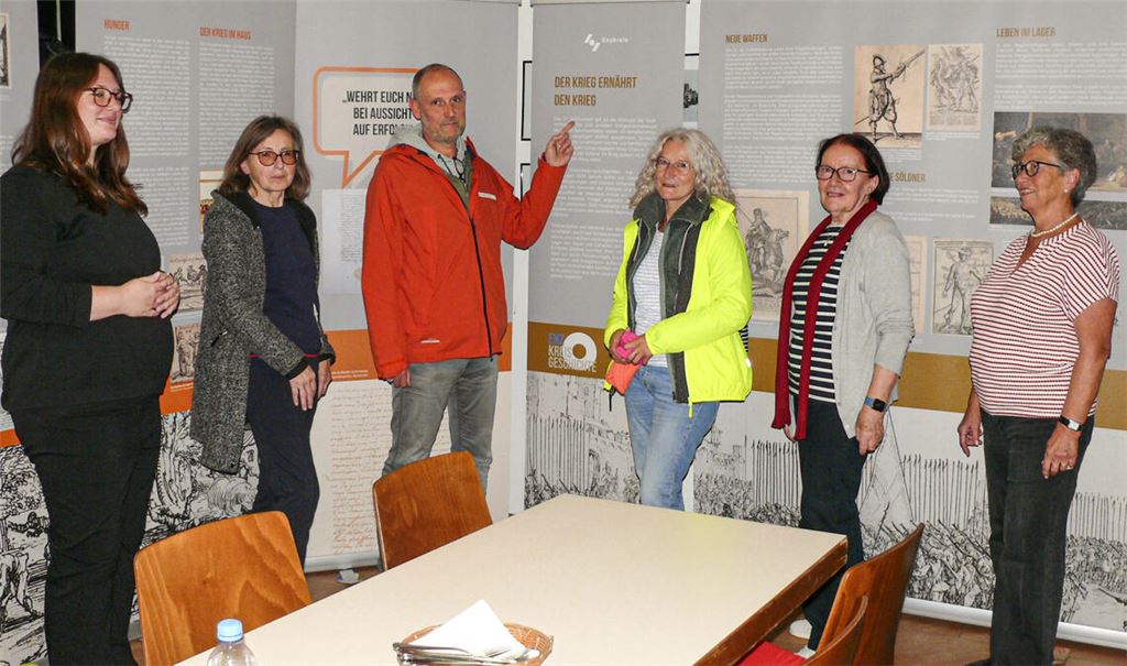 Auf Roll-ups, die im Dorfgemeinschaftsraum aufgestellt sind, informiert die Wanderausstellung über Leid und Elend des Dreißigjährigen Kriegs. Den Eröffnungsvortrag hält Sabine Drotziger (li.) vom Kreisarchiv. Von rechts: Elvira Knothe, Vorsitzende des Heimatvereins und ihre Vize Claudia Martus-Ehrmann mit interessierten Gästen. Foto: Dietrich