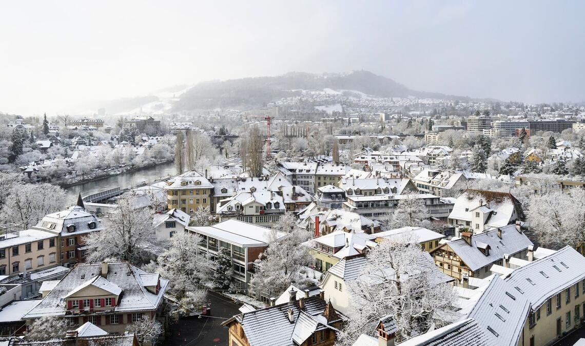 Bern im Winterkleid: Schnee auf Dächern und Bäumen, der Gurten taucht aus leichtem Nebel auf