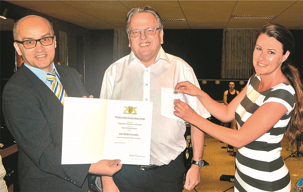 Bürgermeister Harald Eiberger und seine Assistentin Nadine Lengle zeichnen Reimund Scheytt mit der Landesehrennadel aus, während „sein“ Musikverein ein Ständchen beiträgt.Stahlfeld