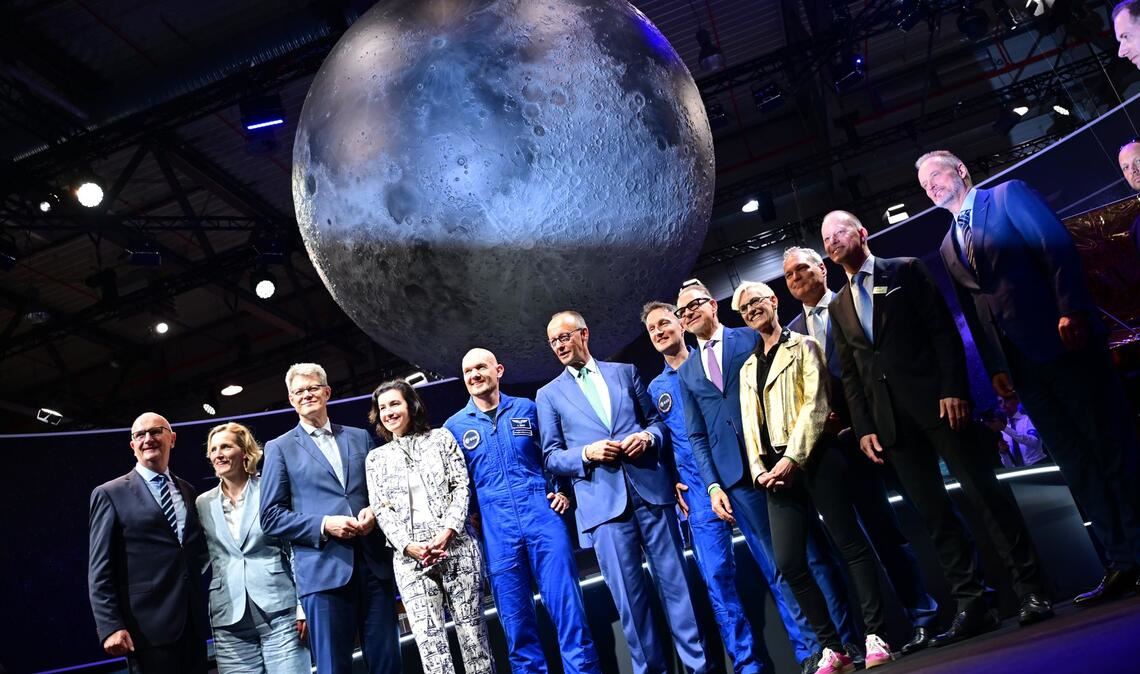 Bundeskanzler Friedrich Merz (6.v.l, CDU) steht unter anderem mit den beiden Esa-Astronauten Alexander Gerst (5.v.l) und Matthias Maurer (7.v.l) während eines Rundgangs auf der Internationalen Luft- und Raumfahrtausstellung (ILA).