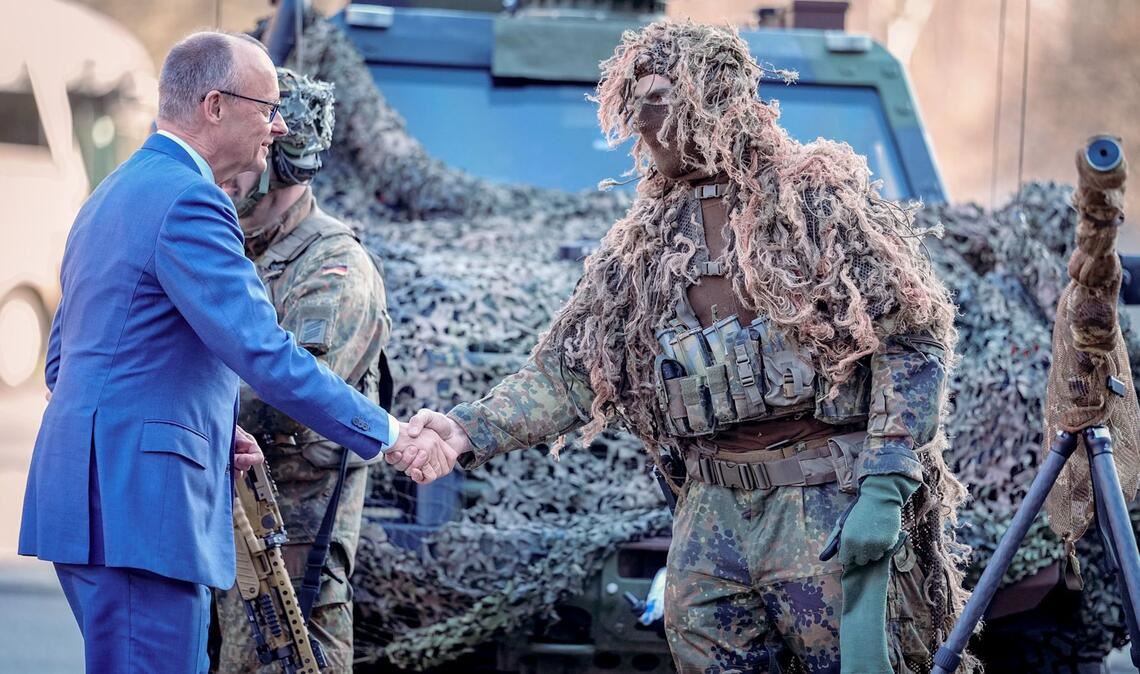 Bundeskanzler Friedrich Merz (l, CDU) wird bei der Verleihung des Fahnenbandes an das Wachbataillon in Berlin von einem Scharfschützen begrüßt.