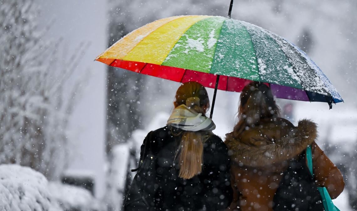 Bunt und grau zugleich: Zwei Frauen gehen mit einem Schirm bei Schneefall in München.