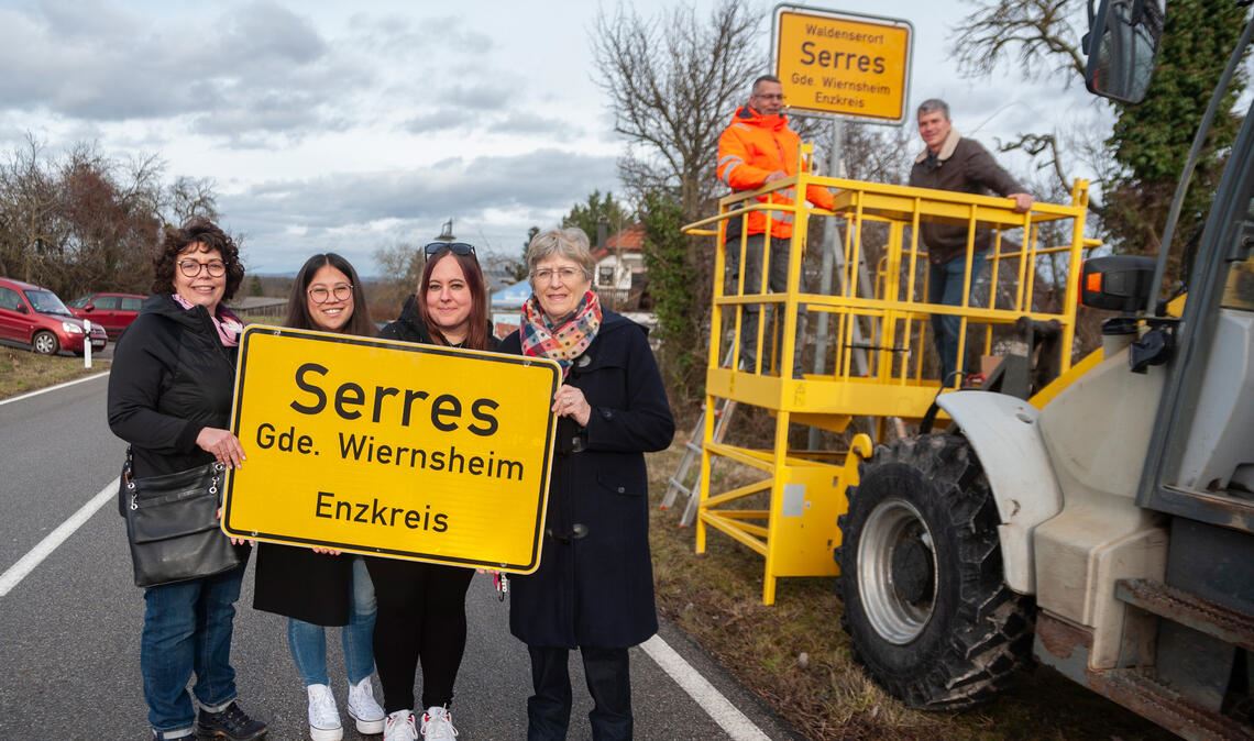 Christine Bauer vom Arbeitskreis Touristik, die Leiterin des Ordnungsamts, Sophie Shum, die Social-Media-Betreuerin der Gemeinde, Heike Jung, Cornelia Schuler vom Museumsstüble (v. li.) und, im Hintergrund, Bauhofleiter Tino Metzger und Bürgermeister Matthias Enz (re.) beim Austausch eines der Ortsschilder des „Waldenserorts“ Serres. Foto: Fotomoment