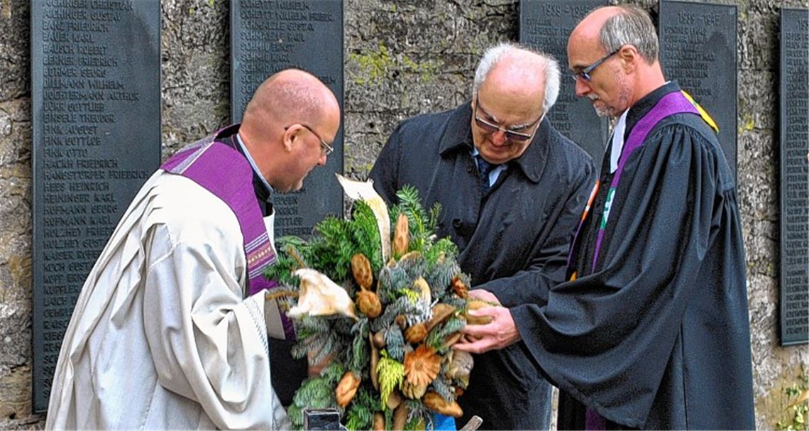 Dekan Claus Schmidt (v. li.), Bürgermeister-Stellvertreter Winfried Scheuermann und Pfarrer Wolfgang Schlecht legen gemeinsam einen Kranz am Ehrenmal nieder.