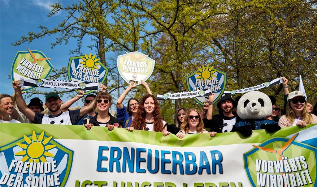 Demonstrierende halten ein Banner und Schilder in die Höhe, darunter eine Person im Pandakostüm.