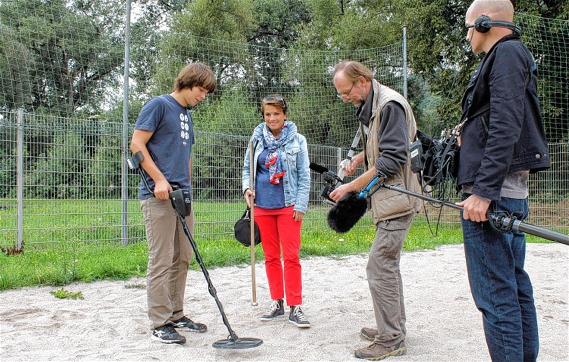 Der 16-jährige Schatzsucher Janik Ratke aus Öschelbronn präsentiert SWR Moderatorin Sonja Faber-Schrecklein, Kameramann Nico Wöhrmann und Tonmann Jens Burger seinen Fund im Sand des Beachvolleyballfelds im Nieferner Freibad. Foto: Tilo Keller