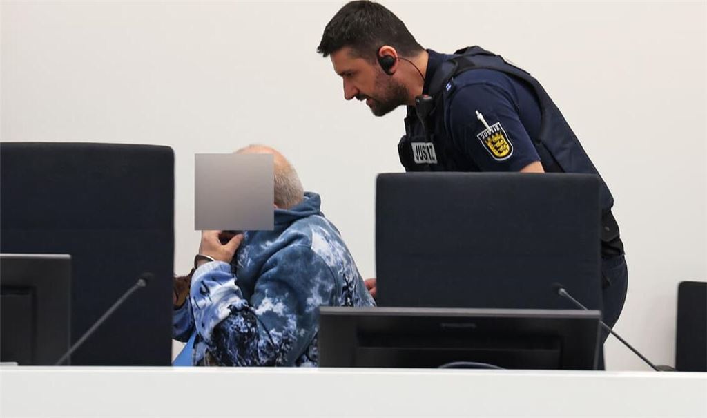Der Angeklagte wird von einem Justizmitarbeiter in den Verhandlungssaal gefahren, er sitzt im Rollstuhl.