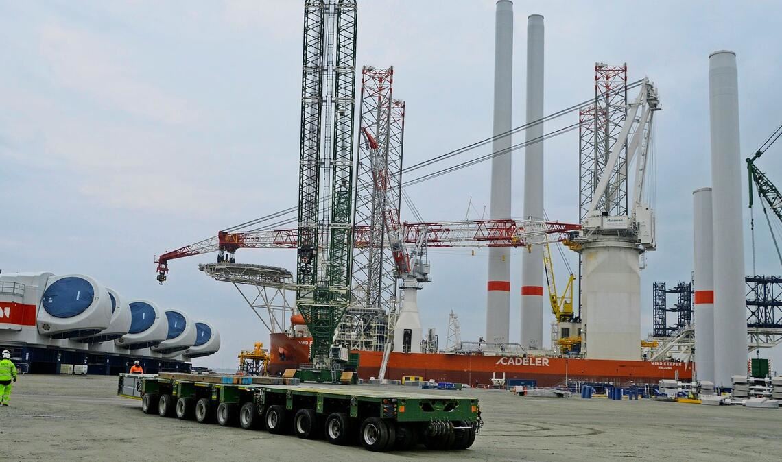 Der Hafen Esbjerg ist Drehkreuz für den Bau des Windparks He Dreiht. Links am Bildrand Maschinenhäuser, im Hintergrund das Errichtungsschiff „Wind Keeper“ mit zwei Türmen an Bord, im Vordergrund ein sogenannter Selbstfahrer (SPMT) für schwere Lasten.