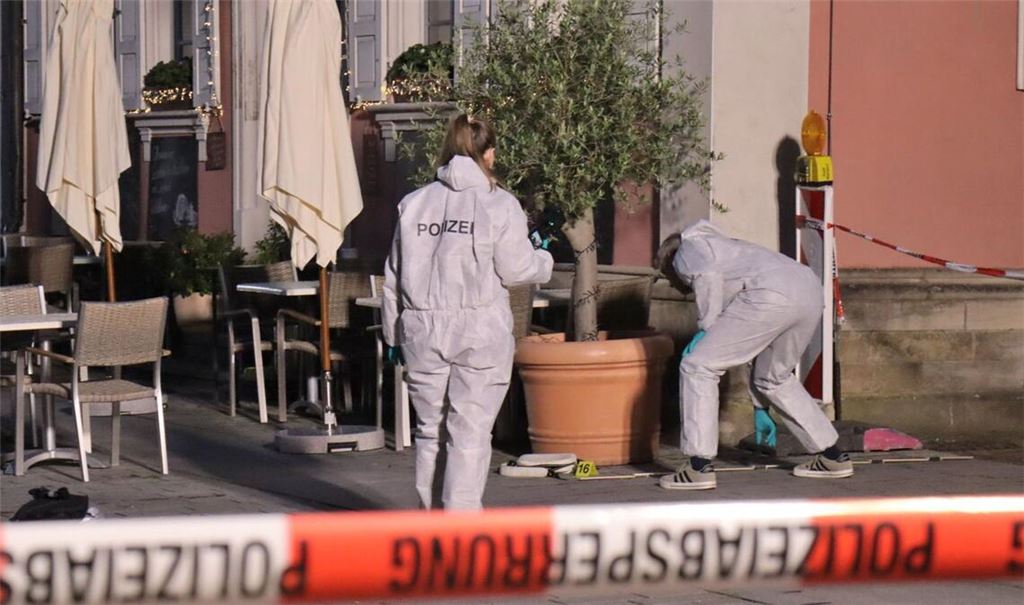 Der Tatort eines nächtlichen Polizeieinsatzes ist mit Flatterband abgesperrt, dahinter Beamte der Spurensicherung im Einsatz.