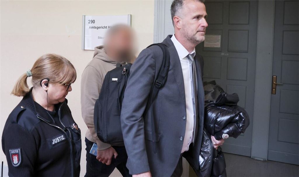 Der Zeuge (Mitte des Bildes) wird von seinem Anwalt (rechts im Bild) in den Gerichtssaal begleitet.