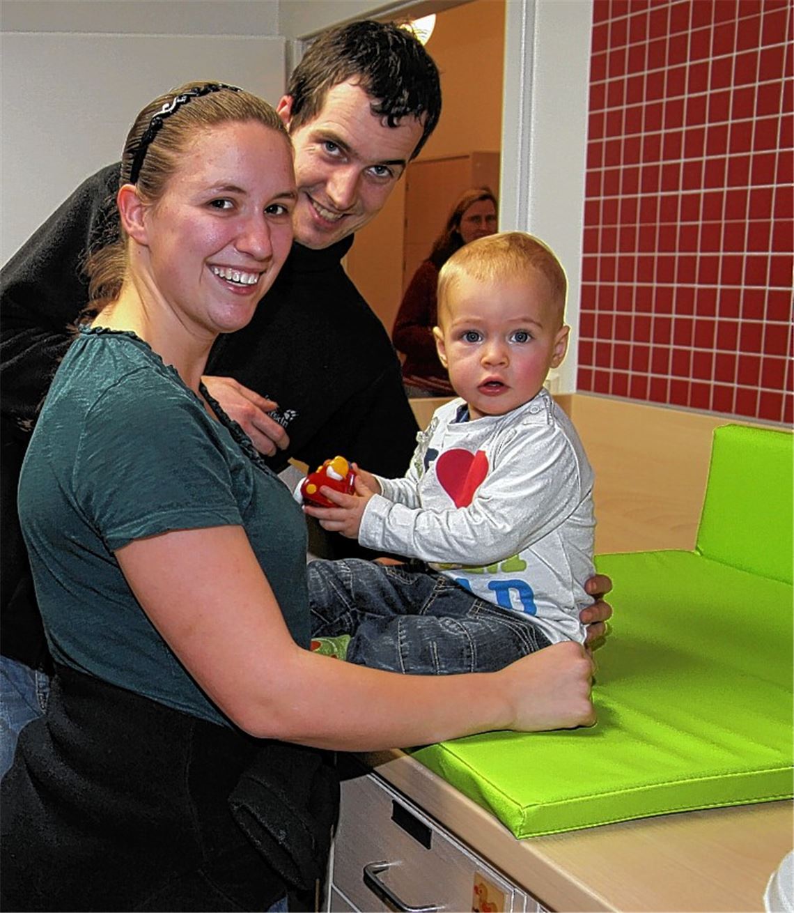 Der kleine Colin-Elias wird am heutigen Mittwoch ein Jahr alt. Am Dienstag hat er schon mal mit Papa Matthias Wildenmann und Mama Angela die Kinderkrippe inspiziert. Rechtes Bild: Pfarrer Hans Veit, Bürgermeister Heinz-Peter Hopp und Elternbeiratsvorsitzender Christian Weiss (v. li.) stellen sich mit jungen und älteren Teilnehmern der offiziellen Einweihung zum Gruppenbild. 