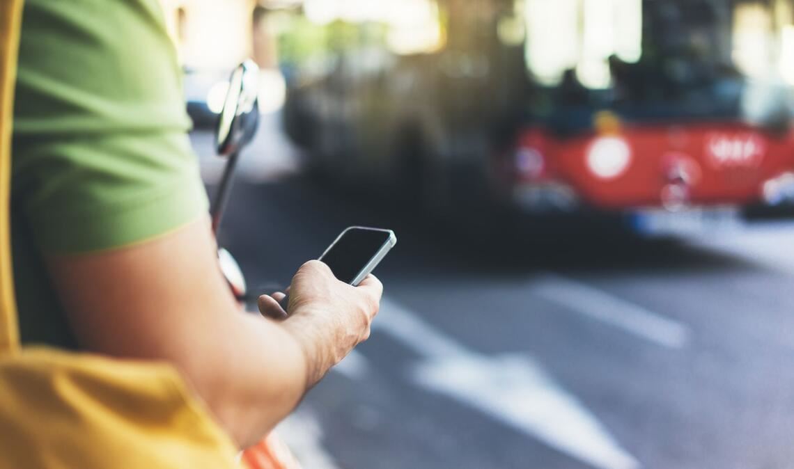 Der typische Griff an der Haltestelle geht zum Handy.