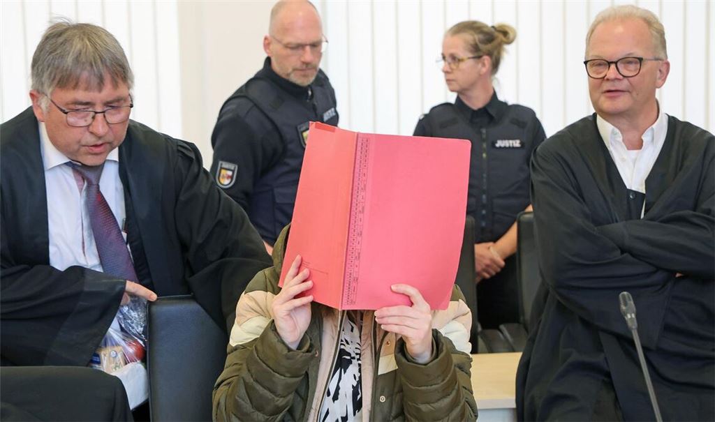 Die Angeklagte sitzt mit Aktendeckel vor dem Gesicht zwischen ihren Verteidigern Andreas Ohm (l-r) und Thomas Löcker.