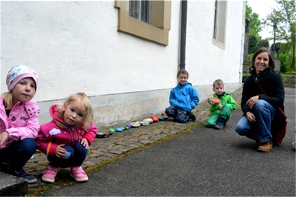 Die Kindergartenkinder Marike (v.li.), Luisa, Jette und Lennart haben ihre bunt bemalten Steine bereits an der Dürrmenzer Kirche abgelegt. Anke Heinrich und Barbara Straub (re.) von der evangelischen St. Andreas-Gemeinde wünschen sich für die Aktion noch viele Nachahmer. Fotos: Stahlfeld
