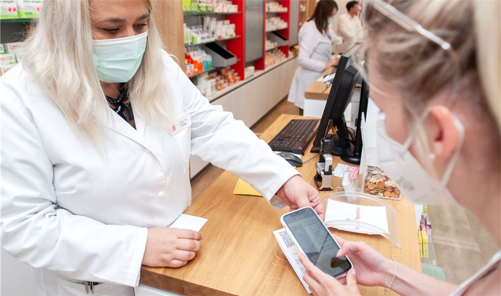 Die Mitinhaberin der Herz-Apotheke, Selma Özer, händigt einer Kundin den digitalen Impfnachweis aus, den sie sich direkt mit einer App aufs Handy lädt. Foto: Fotomoment