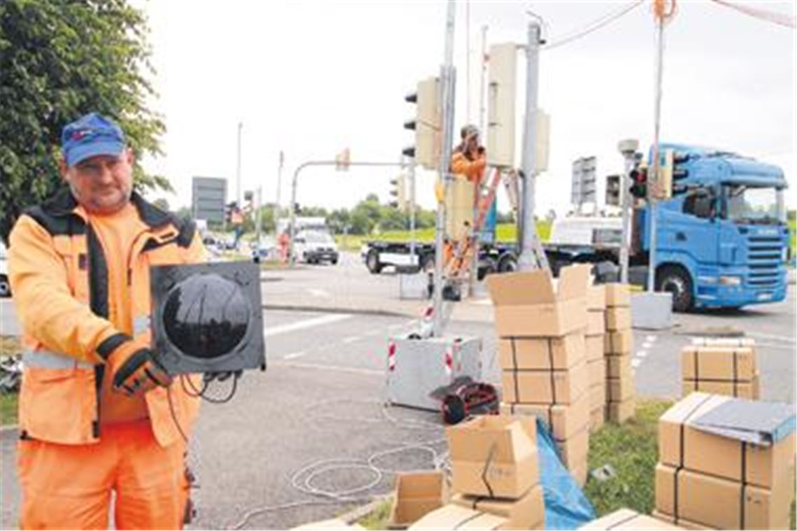 Die Neuen sehen aus wie die Alten: Signalbauer Martin Glauch hält eine mit LED-Technik ausgerüstete Ampel-Leuchte in die Kamera. In den Kartons warten weitere Exemplare auf ihre Montage. Derweil fließt der Verkehr dank der Ersatzsignalanlage am Illinger Eck wie gewohnt. Foto: Disselhoff