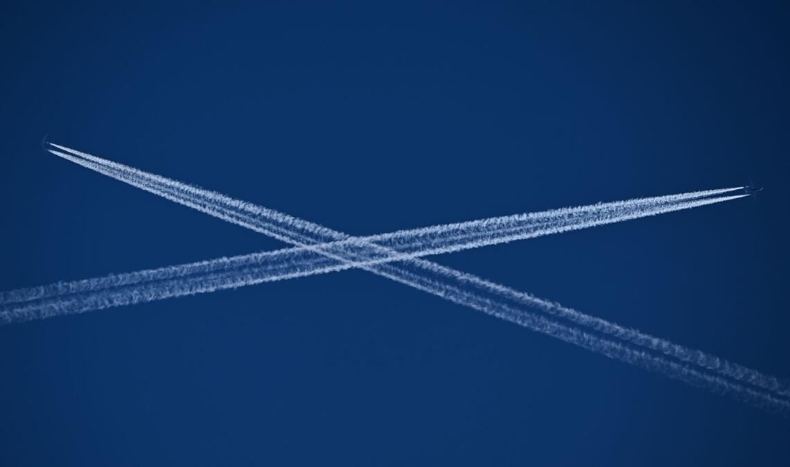 Die Routen zweier Passagiermaschinen, die Kondensstreifen hinter sich herziehen, kreuzen sich am blauen Himmel über Frankfurt am Main.