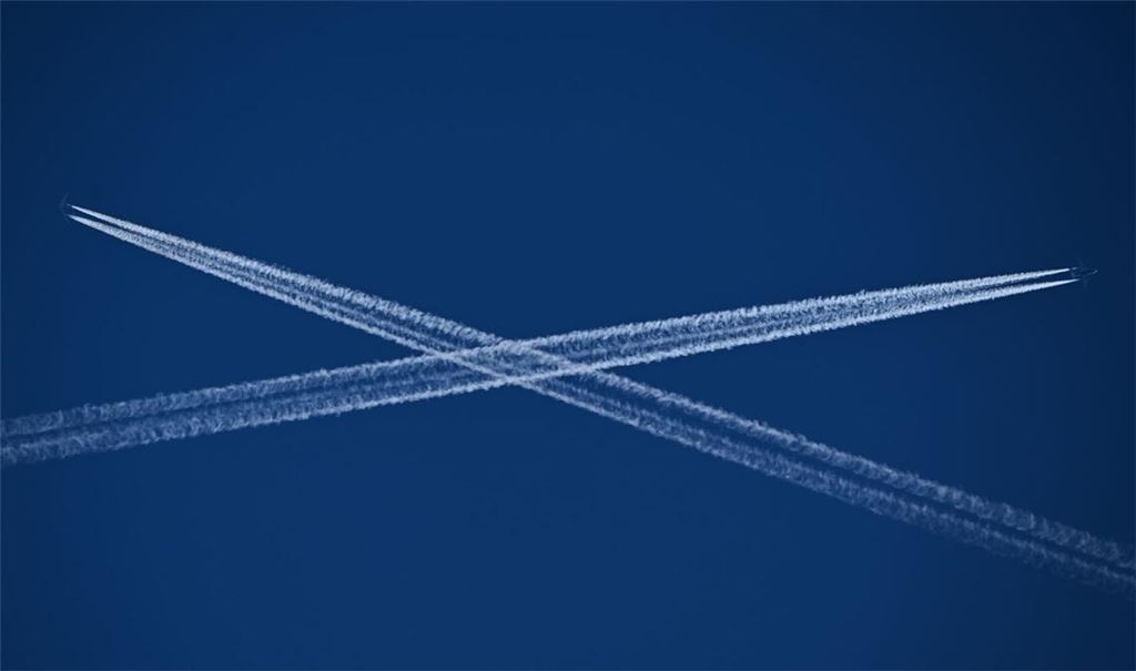 Die Routen zweier Passagiermaschinen, die Kondensstreifen hinter sich herziehen, kreuzen sich am blauen Himmel über Frankfurt am Main.