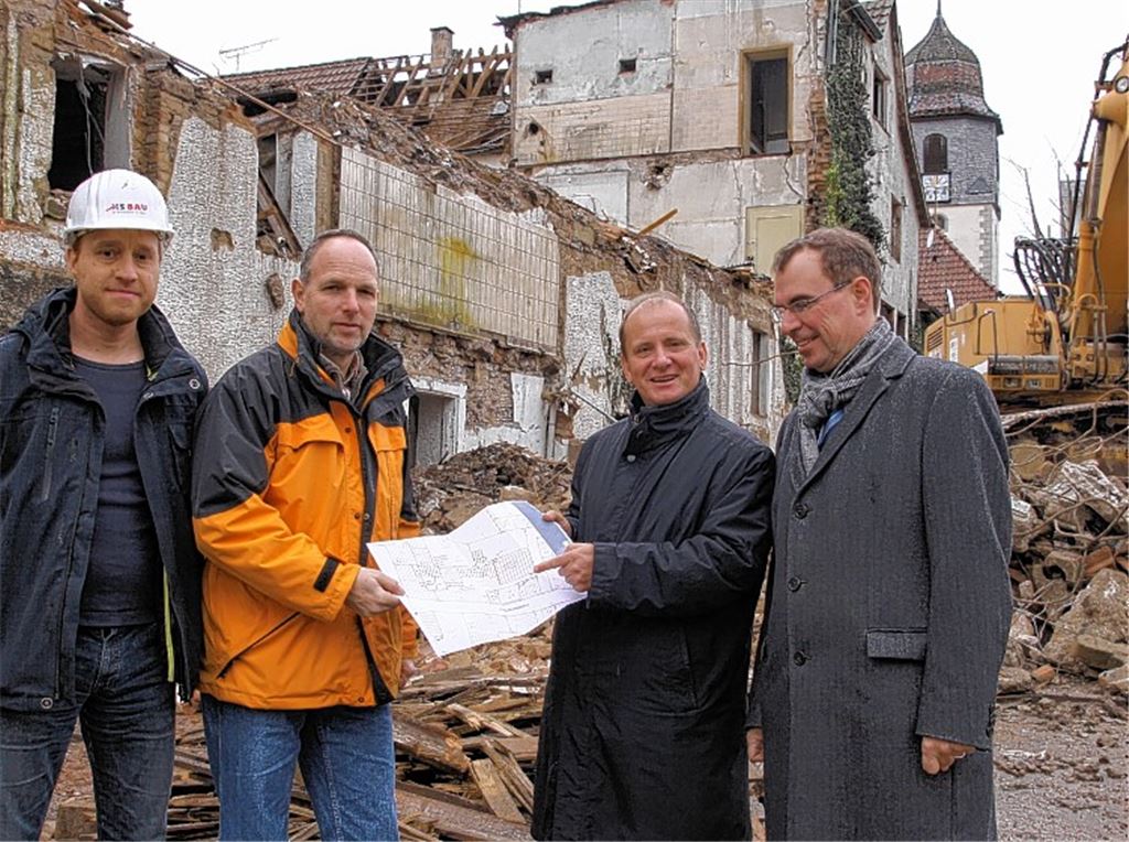 Die Sanierung im Ortskern von Dürrmenz geht weiter. Oberbürgermeister Frank Schneider, Bürgermeister Winfried Abicht und Jörg Soulier vom Tiefbauamt (v. re.) besuchen die Baustelle. Von Bauleiter Stefan Mondon von der Firma HS-Bau werden sie ausführlich über die Abbrucharbeiten auf dem ehemaligen Firmenareal informiert.