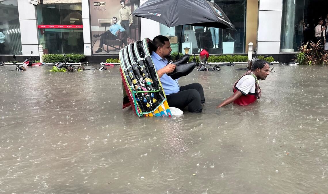 Die Schuhe bleiben trocken: Ein Mann lässt sich in Bangladesch in einer Rikscha durch eine überflutete Straße fahren.