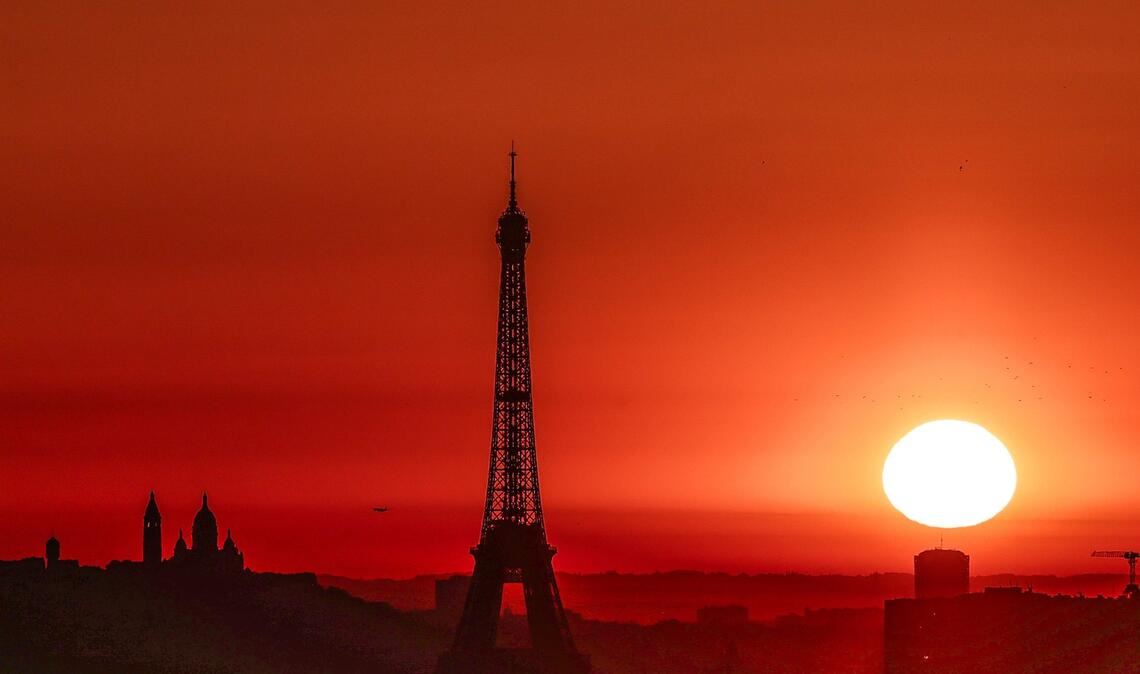 Die Sonne geht Anfang Juli 2025 über dem Eiffelturm und der Basilika Sacre Coeur auf dem Montmartre-Hügel auf, während in der Stadt wegen der hohen Temperaturen Alarmstufe Rot herrscht: