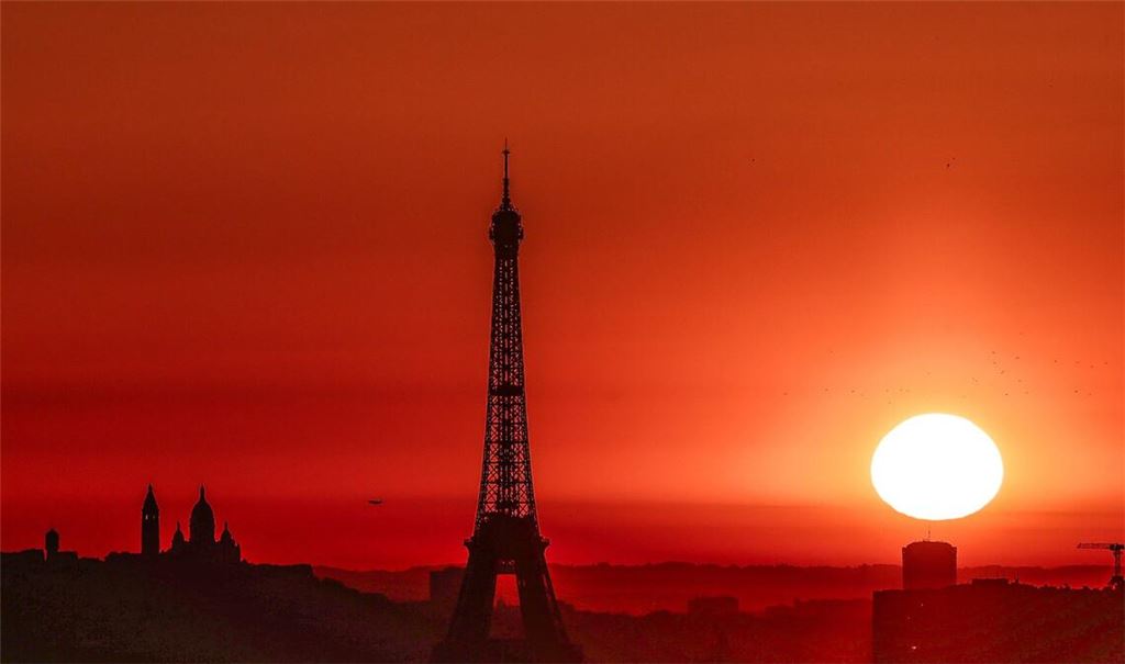 Die Sonne geht Anfang Juli 2025 über dem Eiffelturm und der Basilika Sacre Coeur auf dem Montmartre-Hügel auf, während in der Stadt wegen der hohen Temperaturen Alarmstufe Rot herrscht: