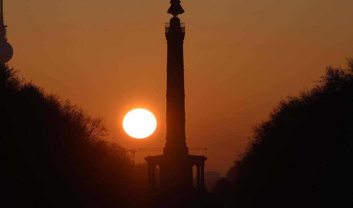 Die Sonne geht am Morgen bei wolkenlosem Himmel hinter der Siegessäule in Berlin auf.