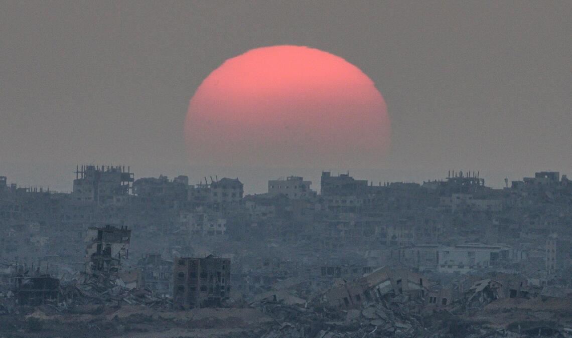Die Sonne geht hinter Gebäuden unter, die bei israelischen Boden- und Luftangriffen im Gazastreifen zerstört wurden, gesehen vom Süden Israels aus.