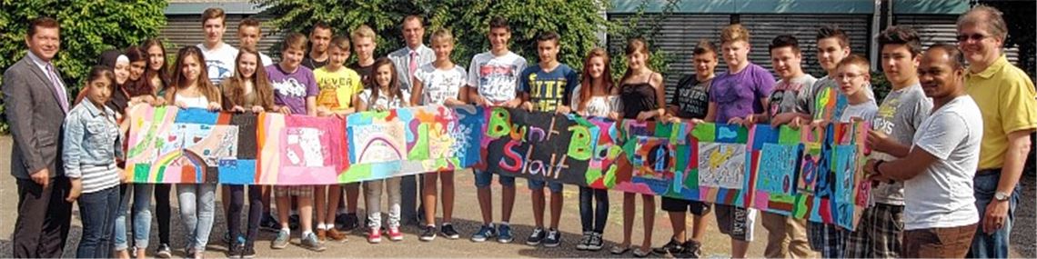 Die UvD-Schüler der Klasse 8a sowie ihre Lehrer Michael Klewar und Michael Blau (v.re.) präsentieren ihr „Bunt statt Blau“-Plakat. Frank Geissler (li.), Leiter der DAK Pforzheim-Mühlacker, freut sich über die rege Teilnahme der Schüler an dem Wettbewerb, den seine Krankenkasse initiiert hat. Mühlackers OB Frank Schneider (hintere Reihe) gratuliert als Schirmherr der Aktion. Foto: Fotomoment