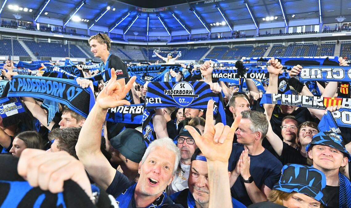 Die Zuschauer im Stadion feiern und halten Schals in die Höhe.