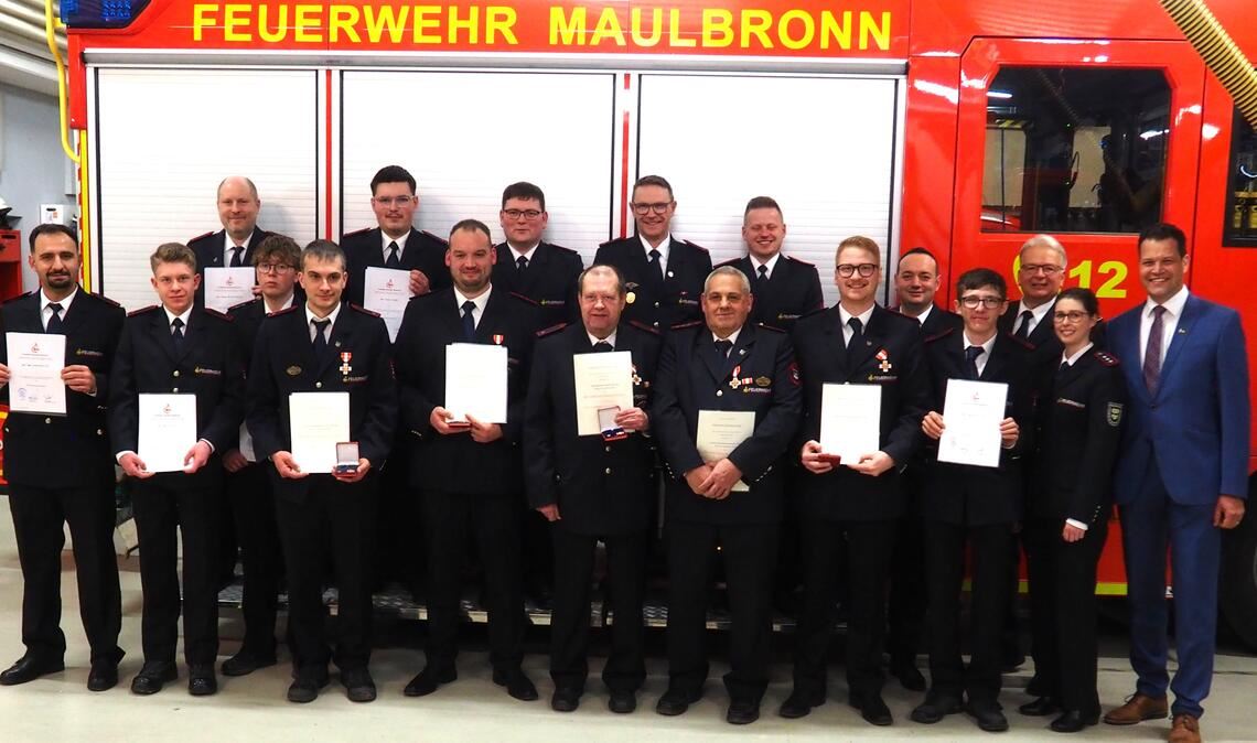 Die beförderten und geehrten Feuerwehrmitglieder zusammen mit (v.re.) Bürgermeister Aaron Treut, Julia Ludwig (Feuerwehrverband Enzkreis), Michael Szobries (stellvertretender Kreisbrandmeister) und Kommandant David Walter (5.v.re.). Foto: Müller