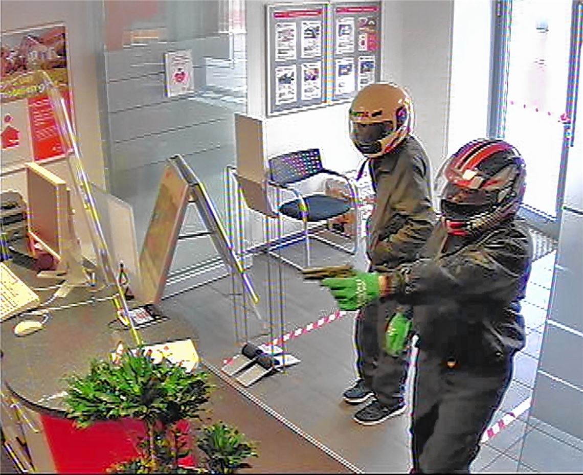 Die beiden Täter bedrohen die Angestellten in der Bank mit dunklen Schusswaffen.pol