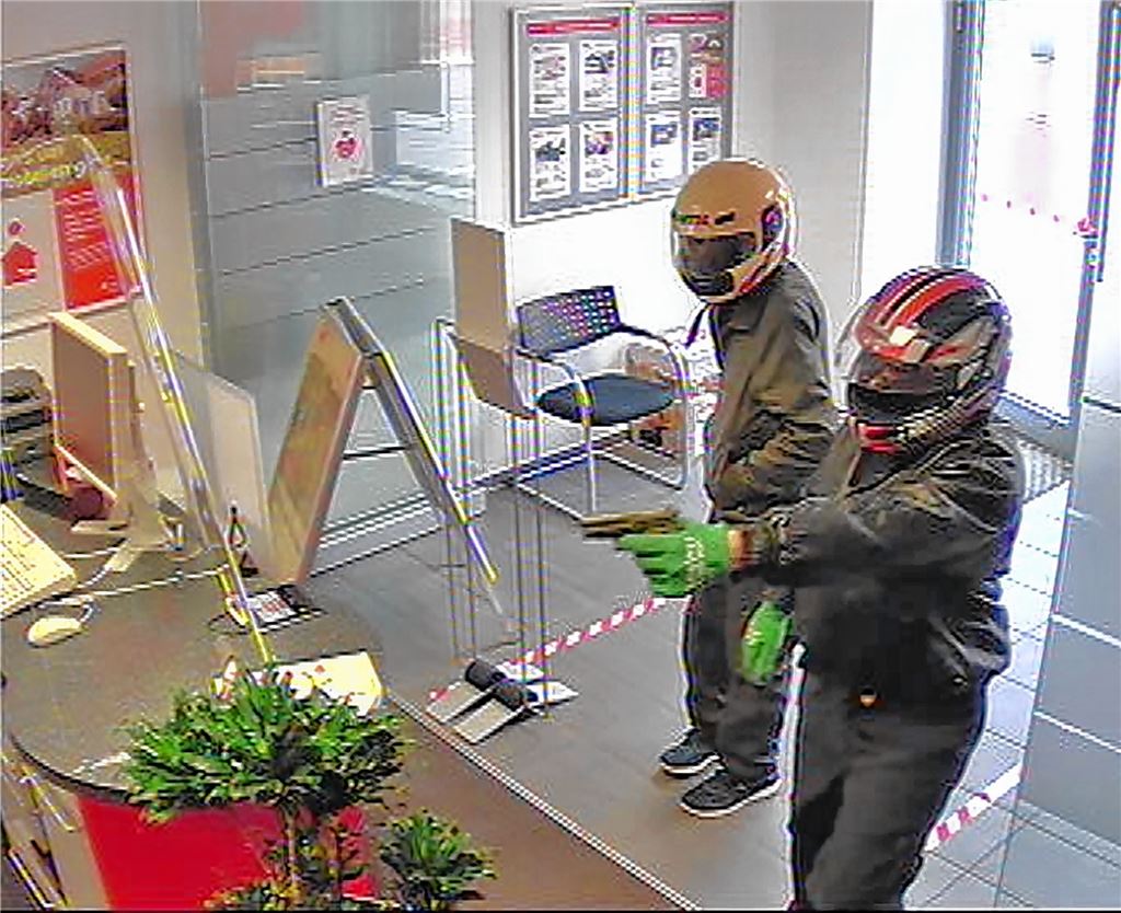 Die beiden Täter bedrohen die Angestellten in der Bank mit dunklen Schusswaffen.pol