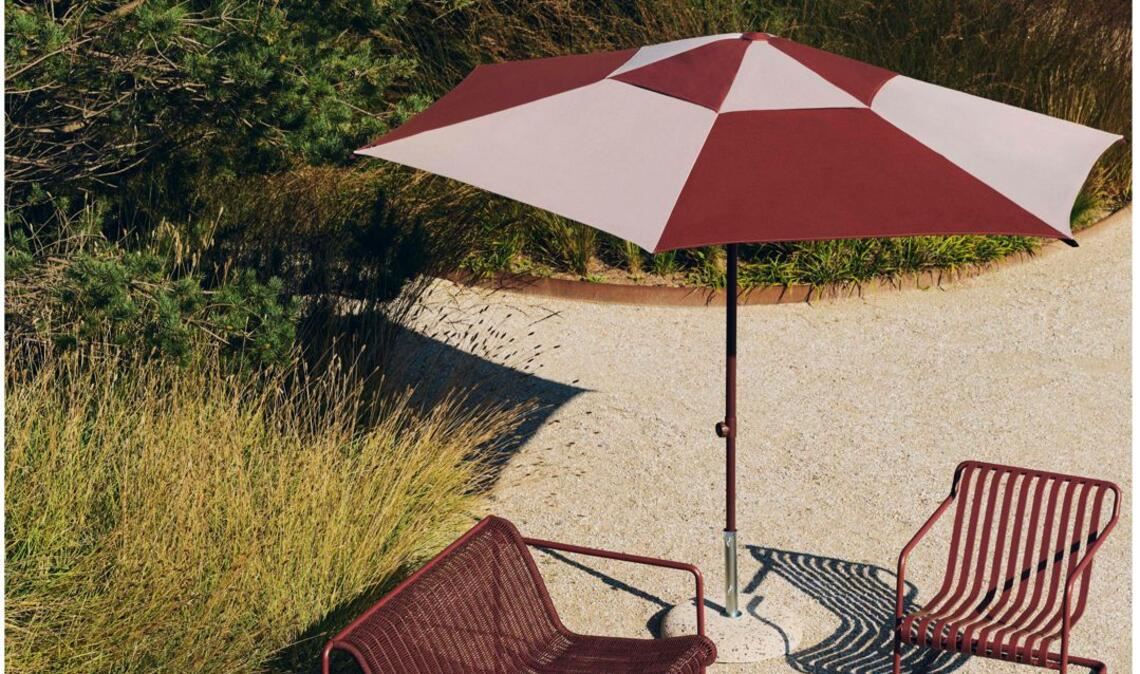 Dunkles Rot und breite Streifen: Der Sonnenschirm ist Teil der Reihe „Terrazza Parasol Square“, die Sessel und Bänke eine Weiterentwicklung der Reihe „Palissade“ name „Cantilever“ von Erwan und Ronan  Bouroullec. Beim Sofa wurden recycelte Polyester-Kabel  in den Stahlrahmen hineingewoben. Auch die Sitzfläche besteht aus Streifen.