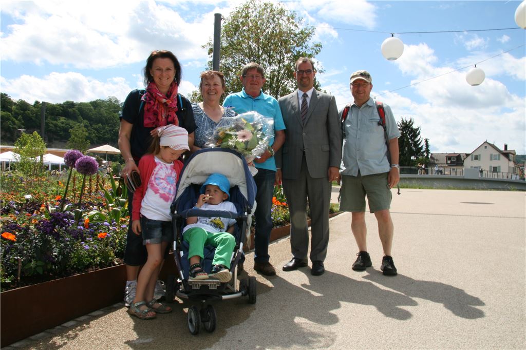 Edith Trost aus Neuffen im Kreise Ihrer Familie (4. v. r.), nachdem sie von Oberbürgermeister Frank Schneider (2. v. r.) als 100.000ste Besucherin der Gartenschau Mühlacker mit einem Blumenstrauß und einem Gartenschauwein überrascht worden war. Foto: pm