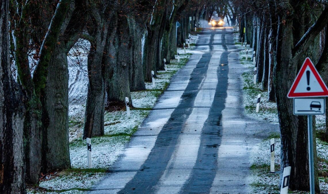 Ein Auto fährt durch eine leicht verschneite Allee. Leichter Schneefall und Temperaturen um die null Grad behindern den Verkehr in Norddeutschland.