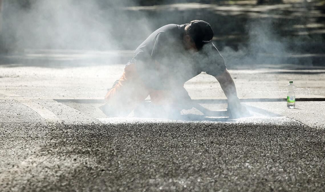 Ein Bauarbeiter repariert eine Straße in Berlin mit Bitumen, einem Bindemittel für Asphalt. (Symbolbild)
