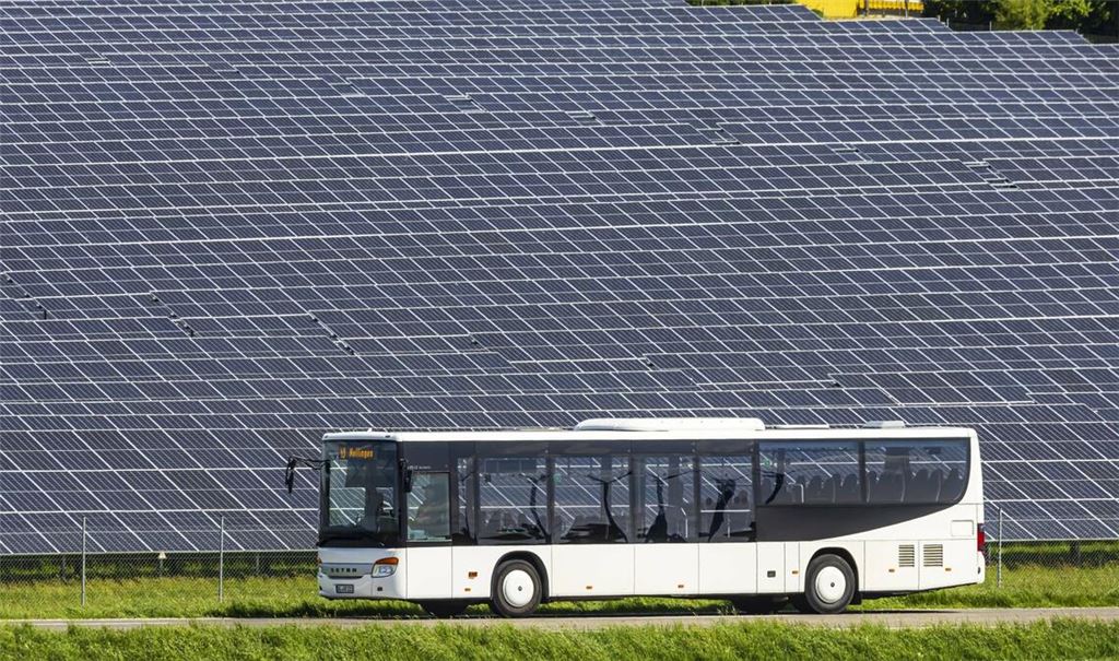 Ein Dieselbus fährt in Nellingen auf der Schwäbischen Alb an einer großen Photovoltaikanlage entlang.