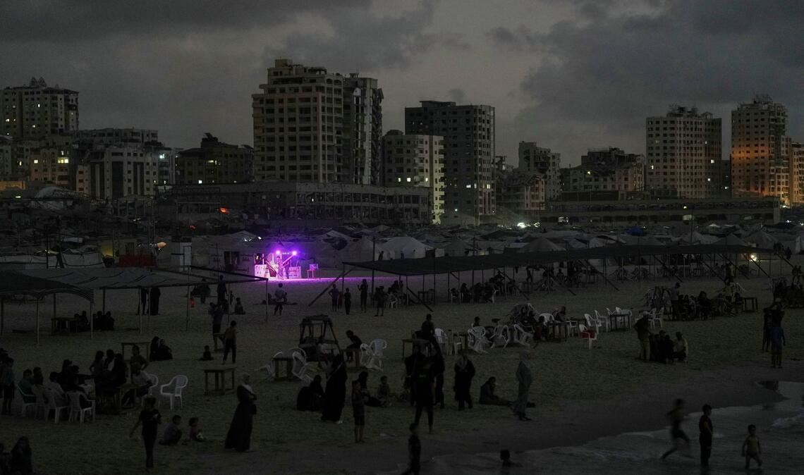 Ein Essensstand leuchtet in der Abenddämmerung, während sich Palästinenser in der Nähe des Hafens von Gaza Stadt im Mittelmeer abkühlen.