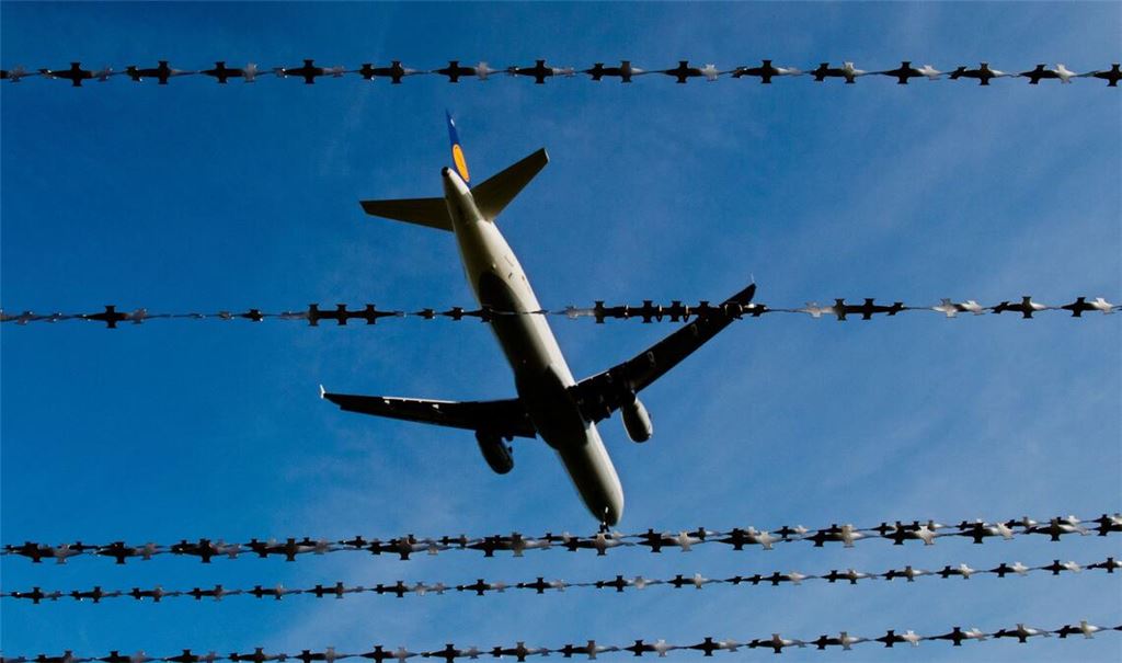 Ein Flugzeug fliegt hinter Stacheldraht. (Symbolfoto)