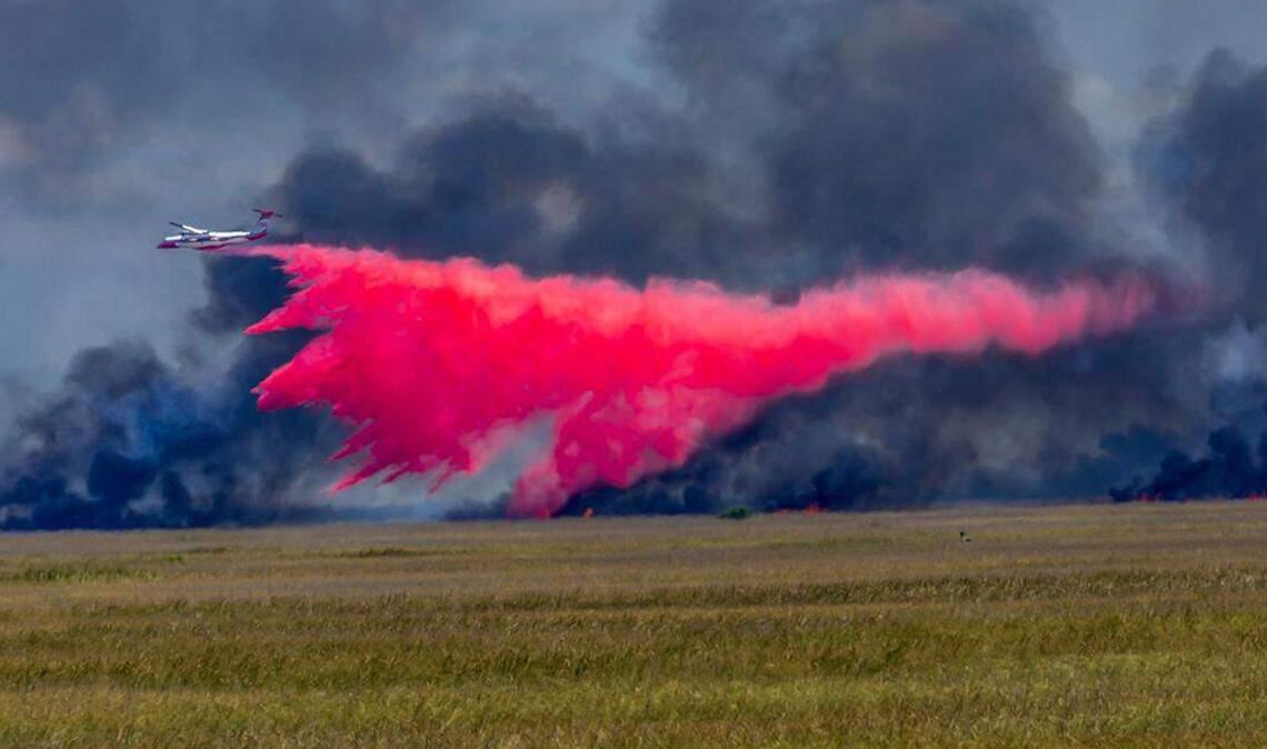 Ein Flugzeug wirft Feuerschutzmittel auf ein großes Waldfeuer.