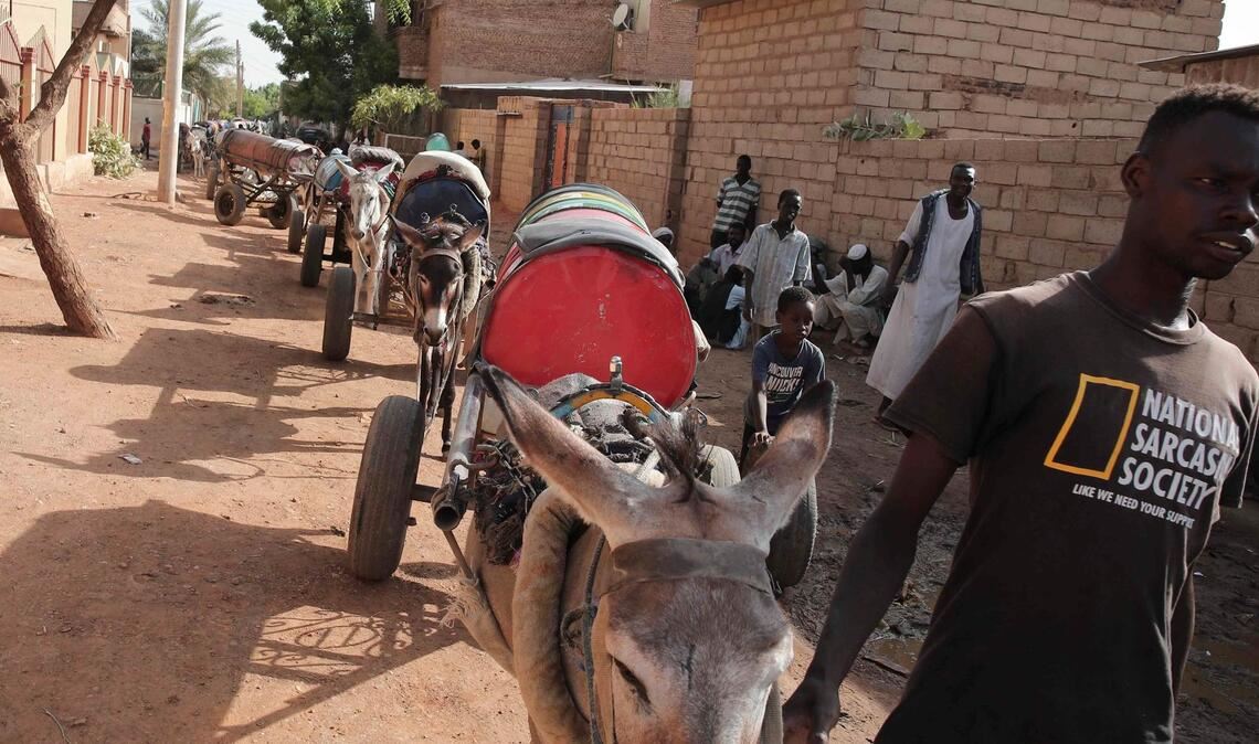 Ein Mann führt in Khartum Esel, die Wasserfässer auf Karren ziehen.